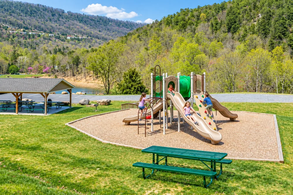 Kids playing on the playground at Massanutten Resort, with the lake and mountains in the background